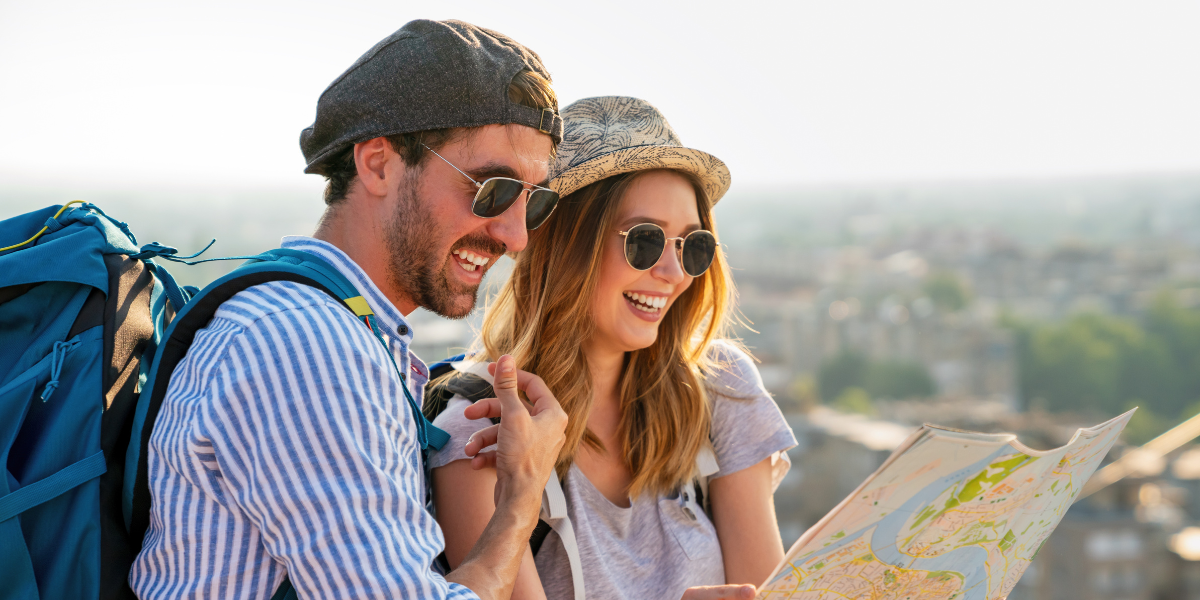 Couple of travelers with backpacks checking a printed map at a city scenic viewpoint.