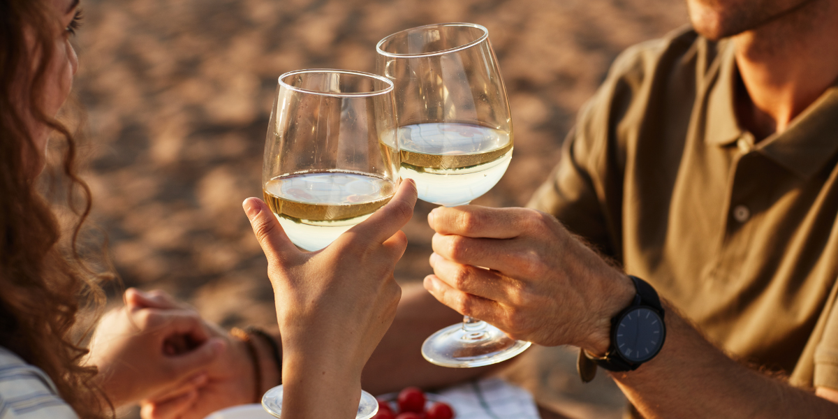 pareja brindando con copas de vino blanco en la playa